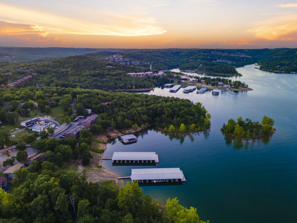 Aerial view of Table Rock Lake near Branson at sunset, with two covered boat docks, a wooded island and resort buildings along the shoreline