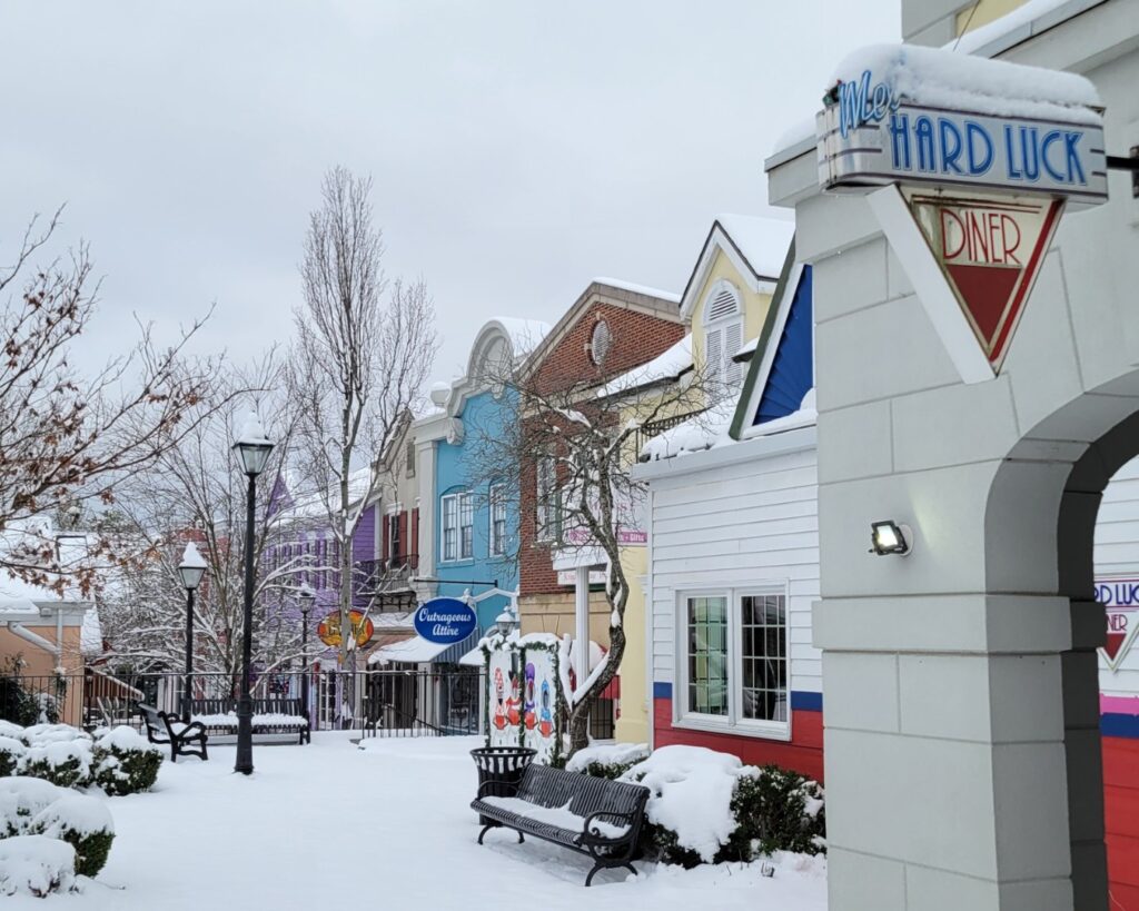 Snow covering a Branson, Missouri shopping street, with colorful storefronts, bare trees and empty benches