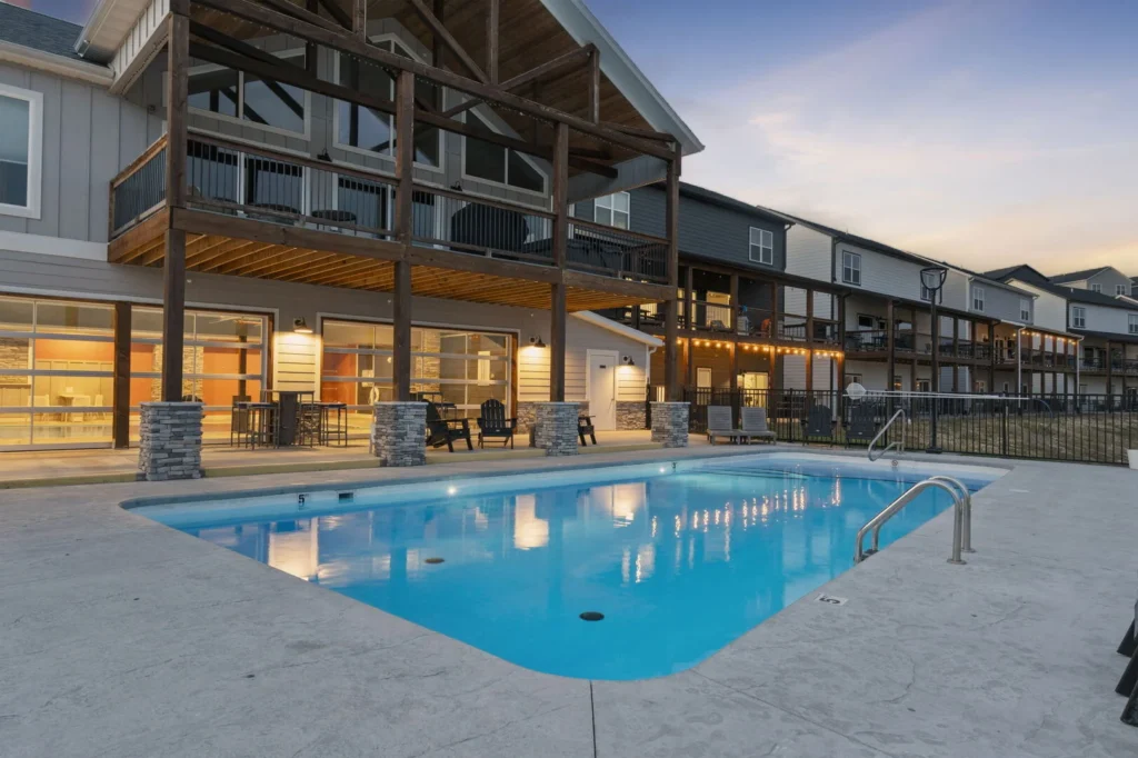 Twilight view of a community outdoor pool with lounge seating in front of modern multi-level Branson vacation townhomes