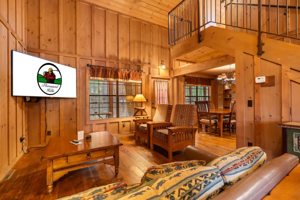 Open cabin living room with vaulted pine walls, a loft overlooking it and a dining table beyond, in a Thousand Hills Vacations rental