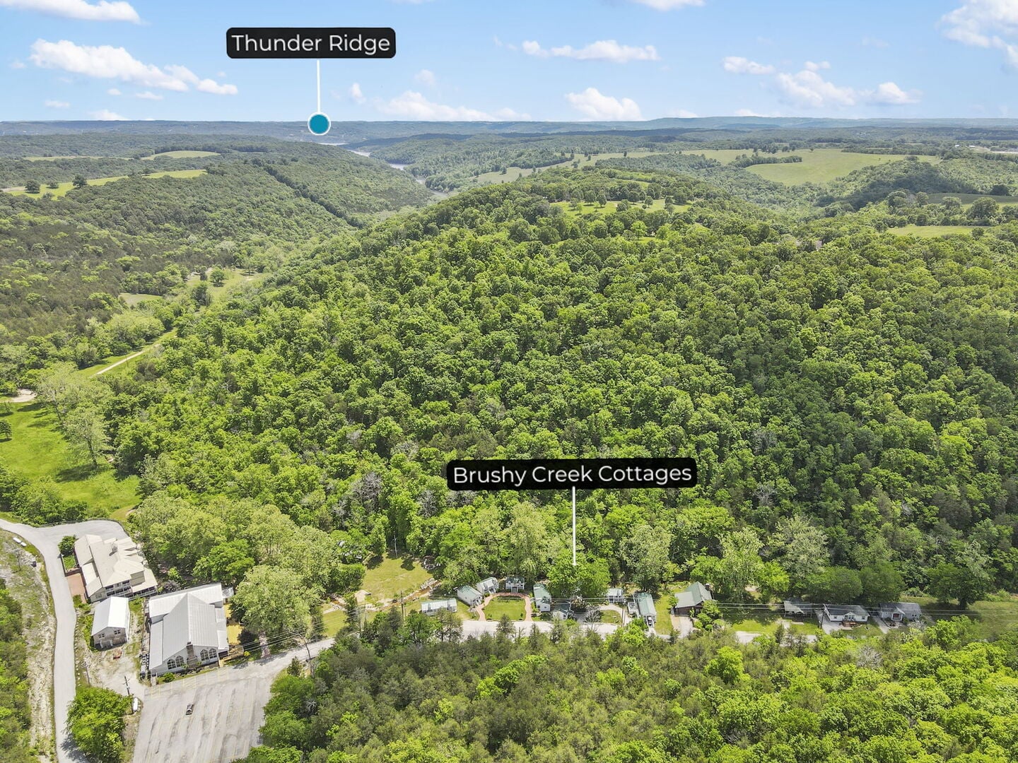 Aerial view of the Cottages at Brushy Creek cluster in a wooded Ozark valley near Branson, Missouri, with a label marking Thunder Ridge on the horizon