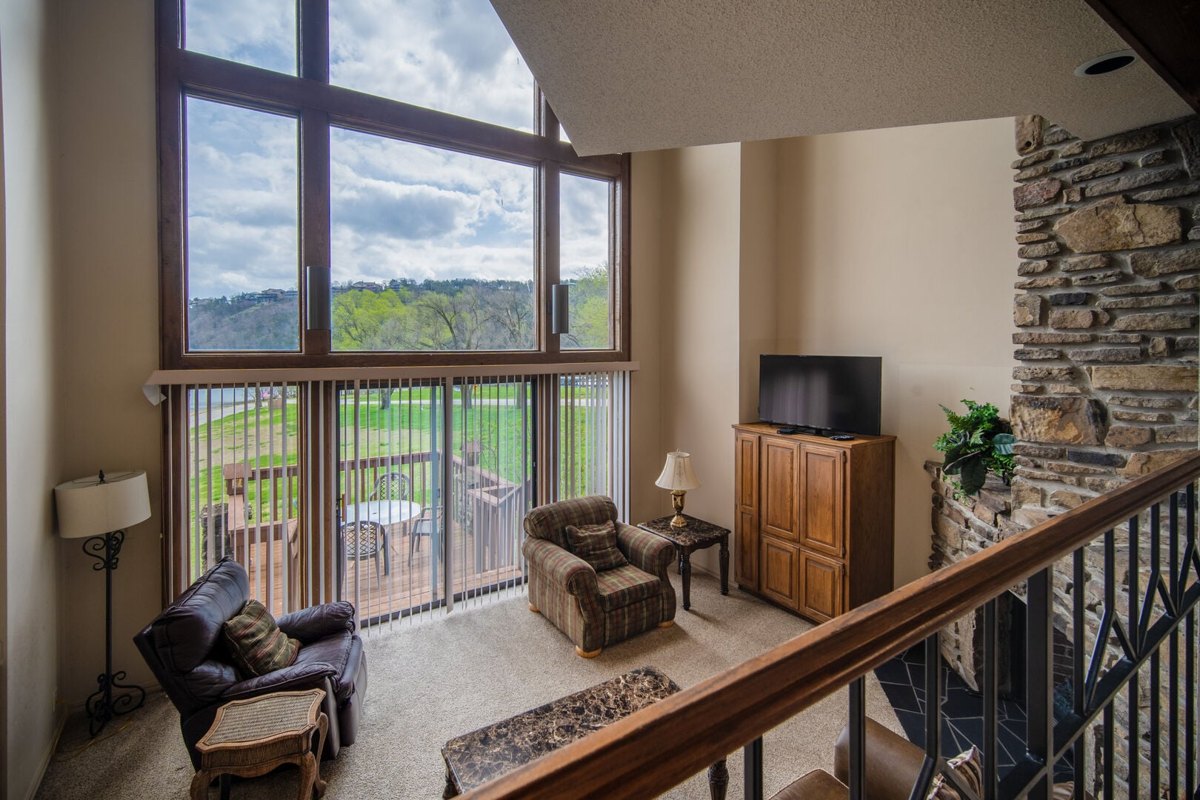 Two-story living room with a stone fireplace and lake-facing windows in a Table Rock Landing two-bedroom condo