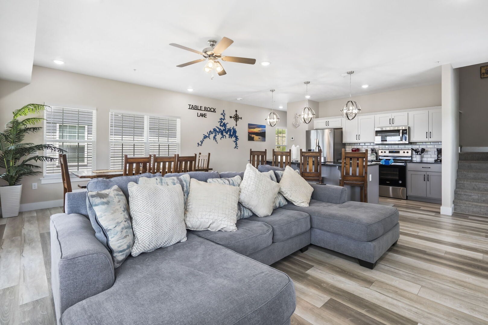 Open plan living room at the Chateau Mountain lodge in Branson, with a grey sectional, a wooden dining table and the kitchen beyond